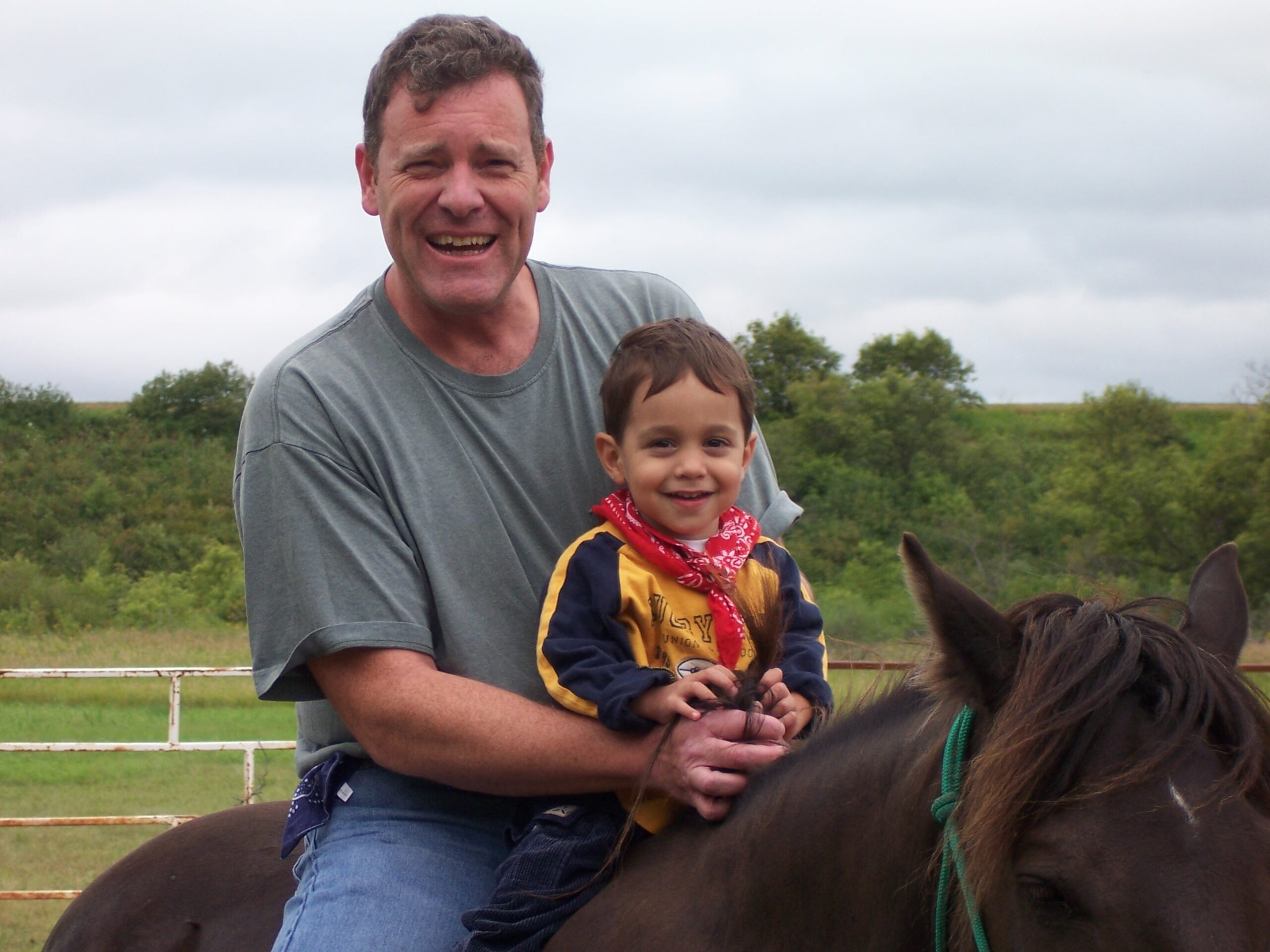 Dad and young son on the back of a horse - they are smiling.